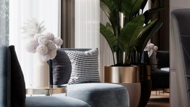 This picture is an interior design rendering of a modern living room. It features a cozy grey couch with two accent chairs in an emerald green and yellow pattern. There is a white coffee table in the center, and a light wood tv unit against the back wall. The walls are painted a neutral beige color, and the windows have bright white shutters. In front of the couch is a large modern rug with a pattern in shades of grey and black. Subtle accents such as a small plant and wall art complete the look.