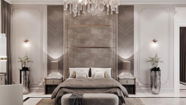 This picture is a rendering of a luxurious modern living room. It features a white and gray color palette throughout, with a light gray velvet sectional sofa and a large round ottoman in the center of the room. On either side of the ottoman, there are two tall armchairs upholstered in gray fabric. Two white coffee tables are situated in front of the sectional sofa, and two mid-century modern style end tables are layered with lamps and decorative accessories. The room is finished with a plush white shag rug, sheer white curtains covering the windows, and