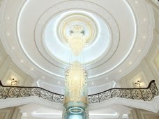 This picture shows a traditional Japanese teahouse set in a peaceful garden. The teahouse is made of wooden panels and has a tiled roof. There are two benches outside the entrance, surrounded by trees and green foliage. There is also a stone lantern in the foreground.