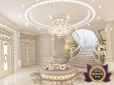 This picture is of a black and white French Bulldog sitting on a blue cushion with its eyes closed. The dog appears to be sleeping peacefully with its nose tucked under its leg and tail curled around its body. The backdrop is a beige wall with shelves displaying a variety of items, including books and home decor.