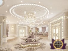 This image appears to show a young, female volleyball player wearing a white jersey and grey shorts about to serve the ball. She is standing on the edge of the court with her head turned towards the other side, ready to hit the ball across the net.